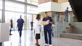 Doctors speaking to each other in a hospital, looking over a file folder.